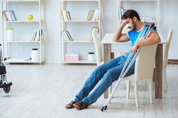 Wall Mural - Young man recovering after surgery at home with crutches and a w