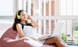 © Natnan - Young woman relaxing on a sofa at home and using laptop of the living room,listening music concept.