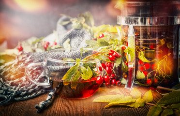 Wall Mural - Cup of healthy tea with scarf, autumn leaves and berries on rustic wooden background.  Hot autumn beverages concept