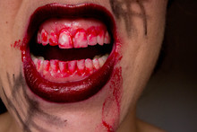 Closeup Of Red Lips Of A Young Girl, With Blood Flowing By. Spooky Woman Smiling, Mouth Of Woman In Blood. Halloween Or Horror Theme.