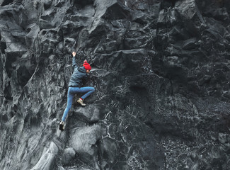 Wall Mural - woman rock climber. rock climber climbs on a black rocky wall on the ocean bank in Iceland, Kirkjufjara beach. woman makes hard move without rope.