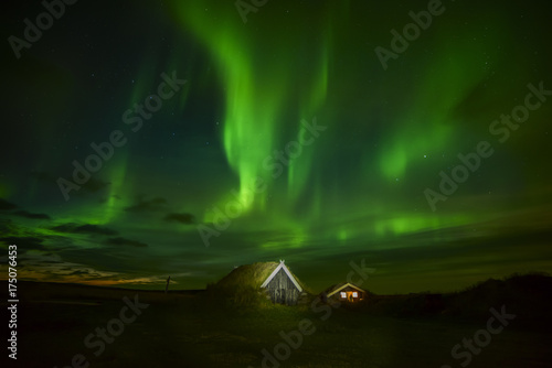 Fototapeta Nocne zdjęcie. Północne światła nad domem w starych tradycjach z trawą na dachu. Islandia.