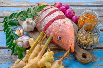 Raw red snapper heads ready for cooking with some spices on wooden cutting board