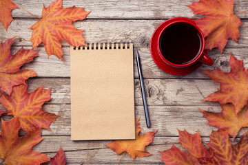 Autumn composition with workspace with blank notebook, pencil, red cup of coffee and beautiful red maple leaves. Top view, flat lay, vintage toning. Autumn relax concept