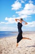 © raisondtre - Closeup portrait of young elegant woman in black dress with white Bolero, dancing barefoot on the sand, on a background of blue sky and white clouds of air.