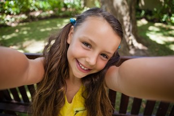 Wall Mural - Portrait of playful girl sitting on bench