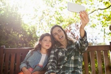 Wall Mural - Happy mother taking selfie with daughter while sitting on wooden