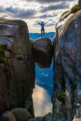 Wall Mural - A woman is standing on the edge of a boulder (Kjeragbolten) stuck in between the mountain crevices of Kjerag above a fjord, near Lysebotn, Norway. The feeling of complete freedom