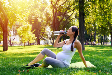 Sportive pregnant woman drinking water in park