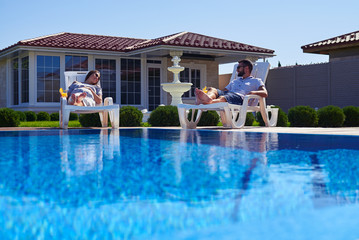 Modern couple getting tan under the sun near pool