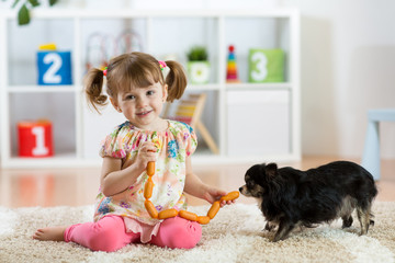 Wall Mural - Kid girl feeds dog on floor in room