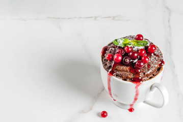 Winter, fall healthy breakfast or snack. The idea of a quick treat for Christmas. Chocolate mug cupkake in ceramic cup, with cranberry and sauce, powdered sugar. White marble table, copy space