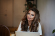 © shurkin_son - Attractive young woman blogger with long wavy hair sitting in modern cafe interior with portable computer, creating content for her personal blog via social media thinking how to attract new followers