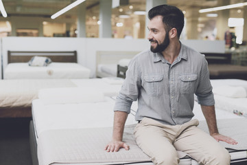 A man in a large store chooses a mattress for himself. He sat down on him to try it out