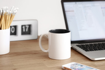 Telework desk at home office in the morning with mug, laptop, phone, clock, and pens