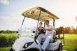 © VadimGuzhva - Happy man and woman are sitting in a white golf cart, which stands on the road of a golf club