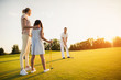 © VadimGuzhva - Family playing golf at sunset. A woman and a girl are looking at a man who is preparing to make a hit