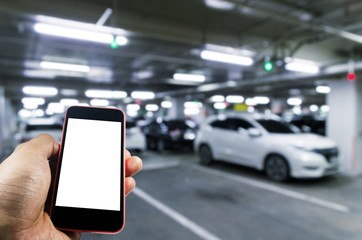 hand using mobile smart phone with blurred image of indoor car parking garage area, RFID solution management system, internet, social media and car parking sensor technology concept