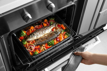 Woman cooking fish with vegetables in oven