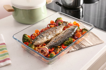 Baking tray with tasty fish and vegetables on kitchen table