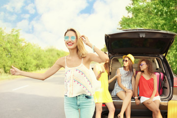 Wall Mural - Young woman with her friends hitchhiking on road