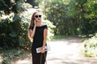 © Romvy - Young business lady in black dress and glasses with coffee and a bag walking in the park