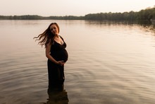 Beautiful Pregnant Woman Standing In Shallow Water At Sunset, Flipping Hair