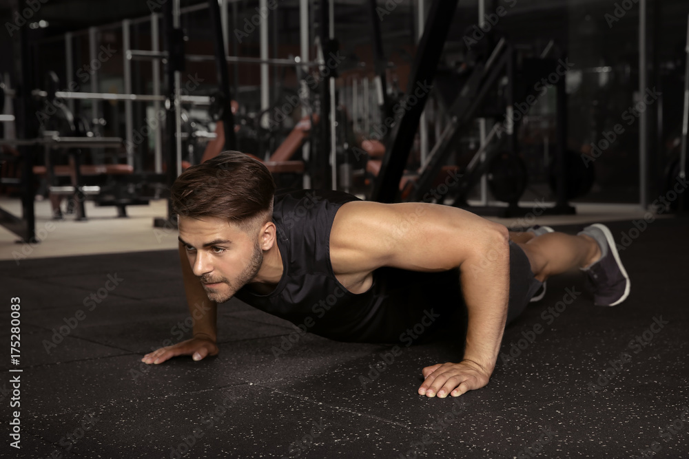 Young sporty man doing push ups in gym