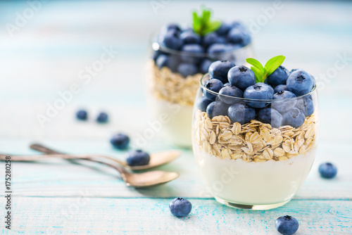Zdjęcie XXL Domowej roboty grecki jogurt z granola i świeżymi czarnymi jagodami w słoju z łyżką na drewnianym tle, selekcyjna ostrość