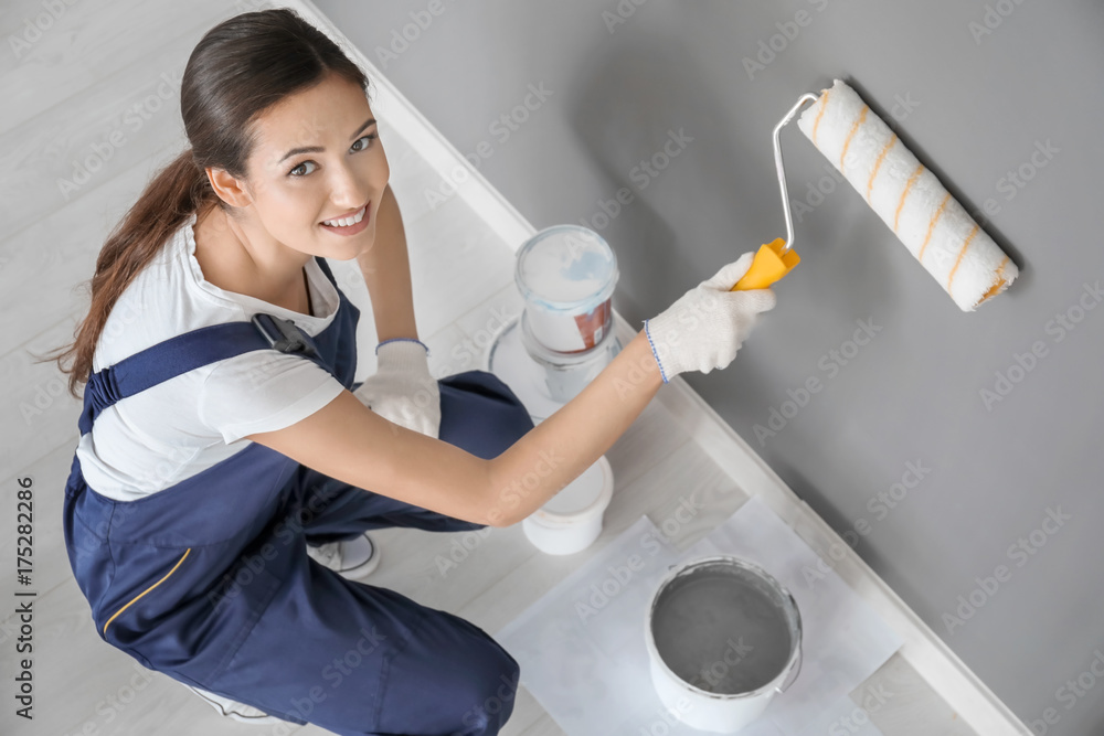 Young female decorator painting wall in room