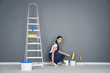 Young female decorator with paint roller near ladder in room