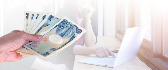 hand woman with Japanese currency yen bank notes on background two woman working on laptop in office