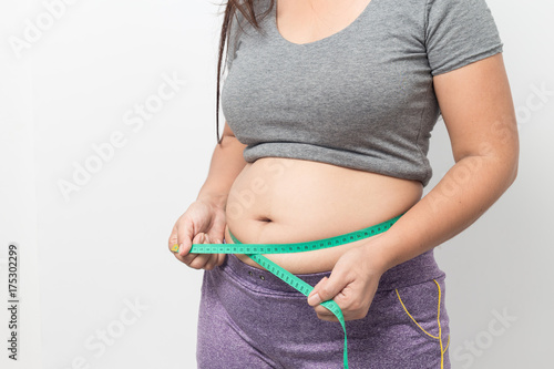 Zdjęcie XXL Z nadwagą kobieta sprawdza out jego ciało sadło z zieloną pomiarową taśmą dla otyłości na szarym tle, Zdrowy pojęcie