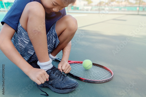Plakat Młody tween Azjatycki chłopiec gracz w tenisa wiąże w górę jego butów