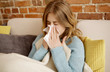 Young woman with cold, flu or allergy blowing nose in paper tissue.