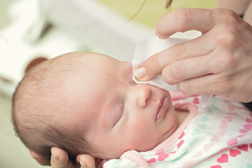 mother cleaning eyes of a newborn baby with physiological solution on a cotton strip; baby's stork b