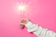Sparkling Bengal fire in a woman's hand on a pink background. Christmas Concept