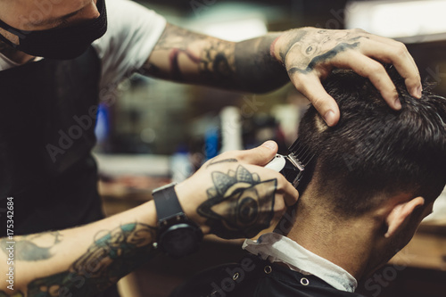 Fotografie, Obraz Crop tattooed stylist concentrated on shaving man with machine doing hairstyle