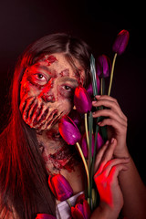 Wall Mural - A zombie girl with sad eyes and a flower of a tulip in hands on a red black background, an image of a Halloween