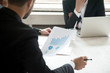 © fizkes - Rear close  up view of project manager holding financial report. Employee presenting rising graph, positive investment result to coworkers during briefing. Team discussing new investment opportunities
