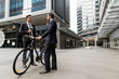 © Sergey Nivens - Two young businessmen with a bike in city centre