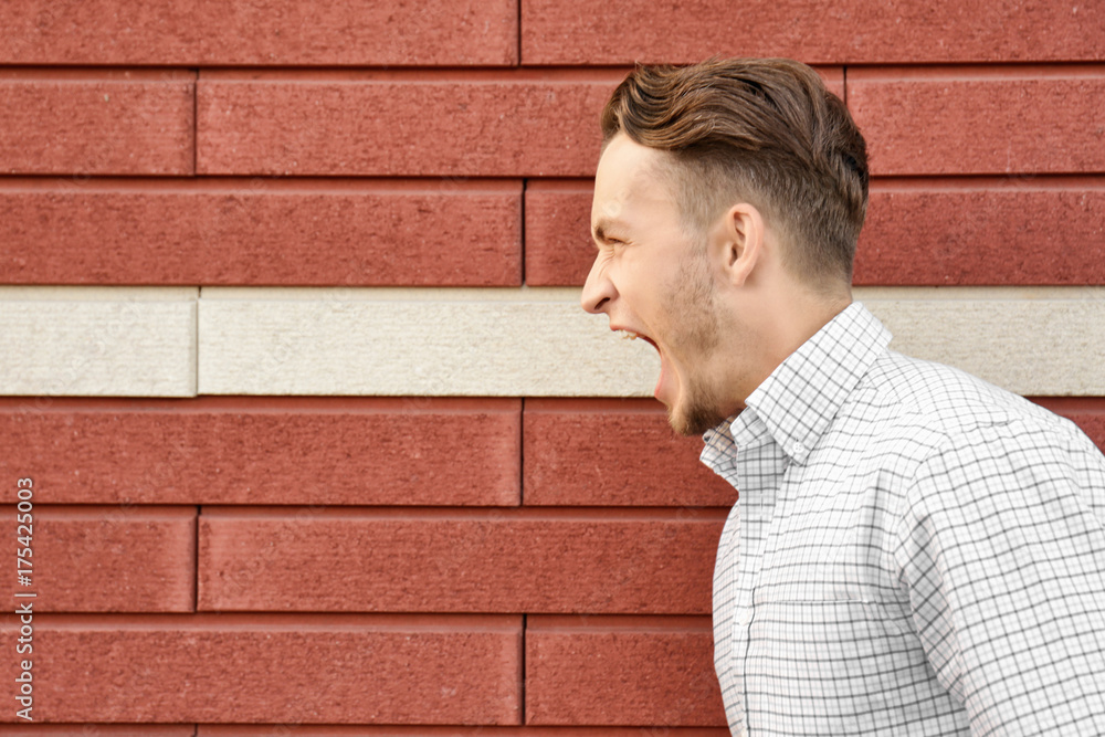 Young emotional man on brick wall background