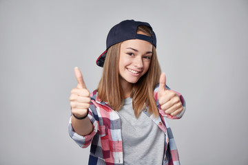 Emotional teen girl giving double thumb up over grey background. Closeup portrait, shallow depth of field, focus on girl