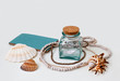 Dreams of sea vacation. Still life composition on white background with sea shells, beads necklace, glass bottle, paper ship and a craft paper notebook with turquoise cover. 