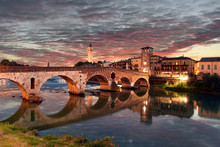 Roman Empire Ancient Bridge Ponte Pietra Over The River Adige In Verona, Italy During Sunset With Illuminated Old Town