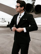 Serious handsome young man in the west and suit walk near plane on the airfield