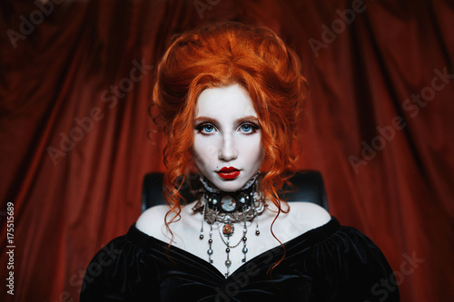 Plakat Kobieta to wampir o bladej skórze i rudych włosach w czarnej sukience i naszyjniku na szyi. Dziewczyna czarownica z pazurami wampira i czerwone usta. Gotycki wygląd. Strój na Halloween.
