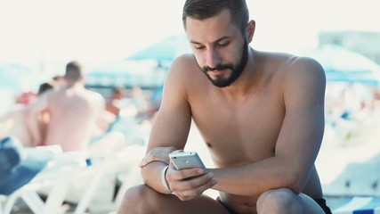 Vacation technology concept portrait young handsome man caucasian using smartphone mobile sea shore beach summer holidays blurred background app travel naked guy brunette beard internet searching rest