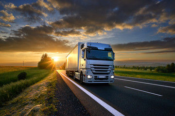 Wall Mural - truck driving on the asphalt road in rural landscape at sunset with dark clouds