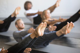 Group of young sporty people practicing yoga lesson with instructor, stretching in Paripurna Navasana exercise, balance pose, working out, indoor close up image, studio, focus on feet
